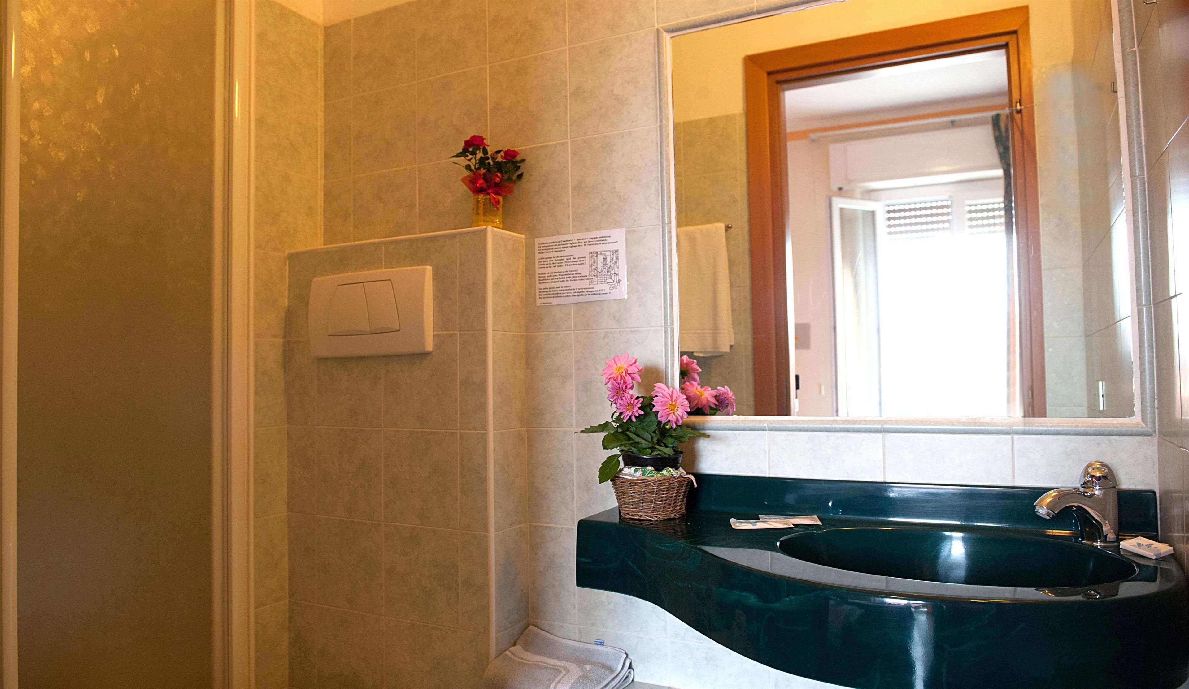 Un baño con un lavamanos verde, un espejo, una ducha y un interruptor de luz en la pared.
