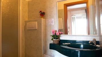 Un baño con un lavamanos verde, un espejo, una ducha y un interruptor de luz en la pared.