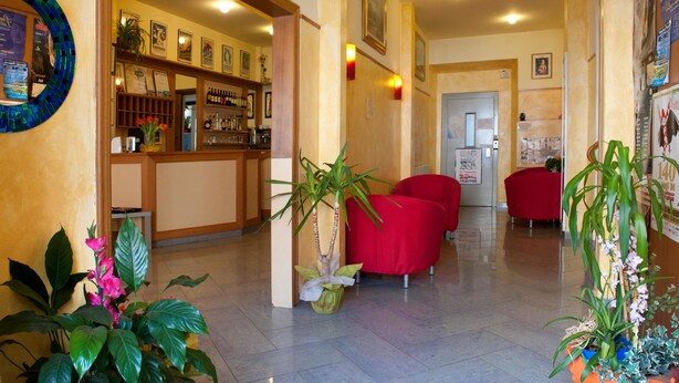 A hotel lobby with a reception desk, red seating, and potted plants. - Hotel Dolly (Viareggio)