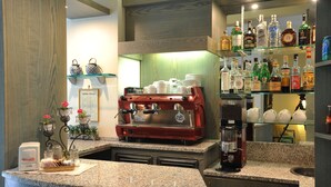 A coffee bar with a red espresso machine, a coffee maker, and a variety of coffee cups and mugs. There are shelves with bottles and a menu on the wall. - Riviera Blu (Pisa)