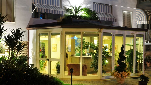 A glass-enclosed building with a roof, surrounded by greenery and potted plants. - Riviera Blu (Pisa)