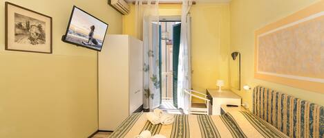 Habitación de hotel con cama, televisión, escritorio con lámpara y baño visible a través de una puerta abierta.
