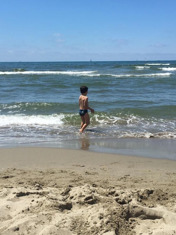 Un niño con bañador caminando por una playa arenosa con olas.
