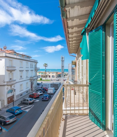 A balcony with a view of a street, parked cars, and buildings in the background.