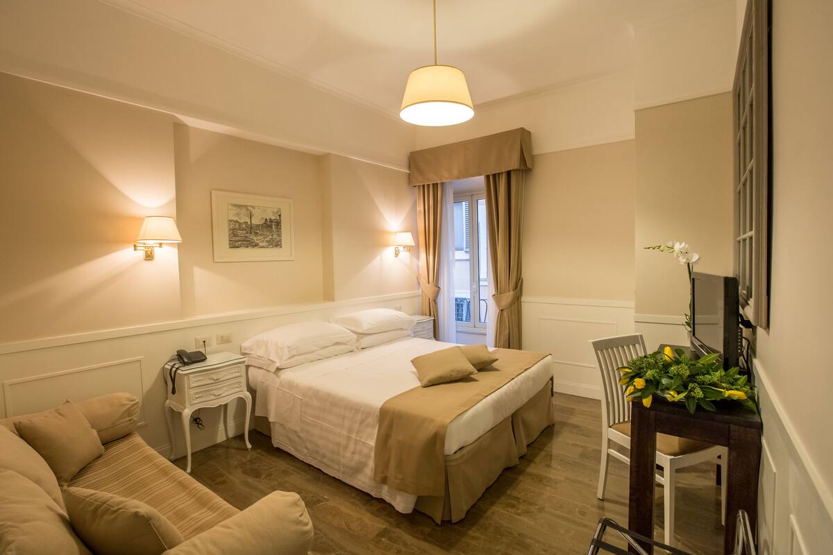 A hotel room with a bed, bedside tables, a desk, a chair, and a television.