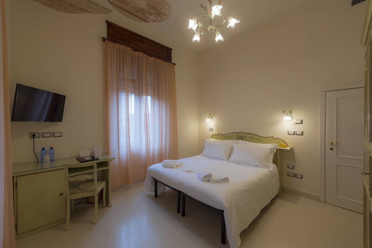 Une chambre d’hôtel avec un lit, un bureau, une télévision et une fenêtre avec des rideaux.