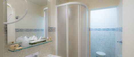 Un baño con lavamanos blanco, repisas de vidrio con artículos de aseo, cabina de ducha y piso con azulejos azules.