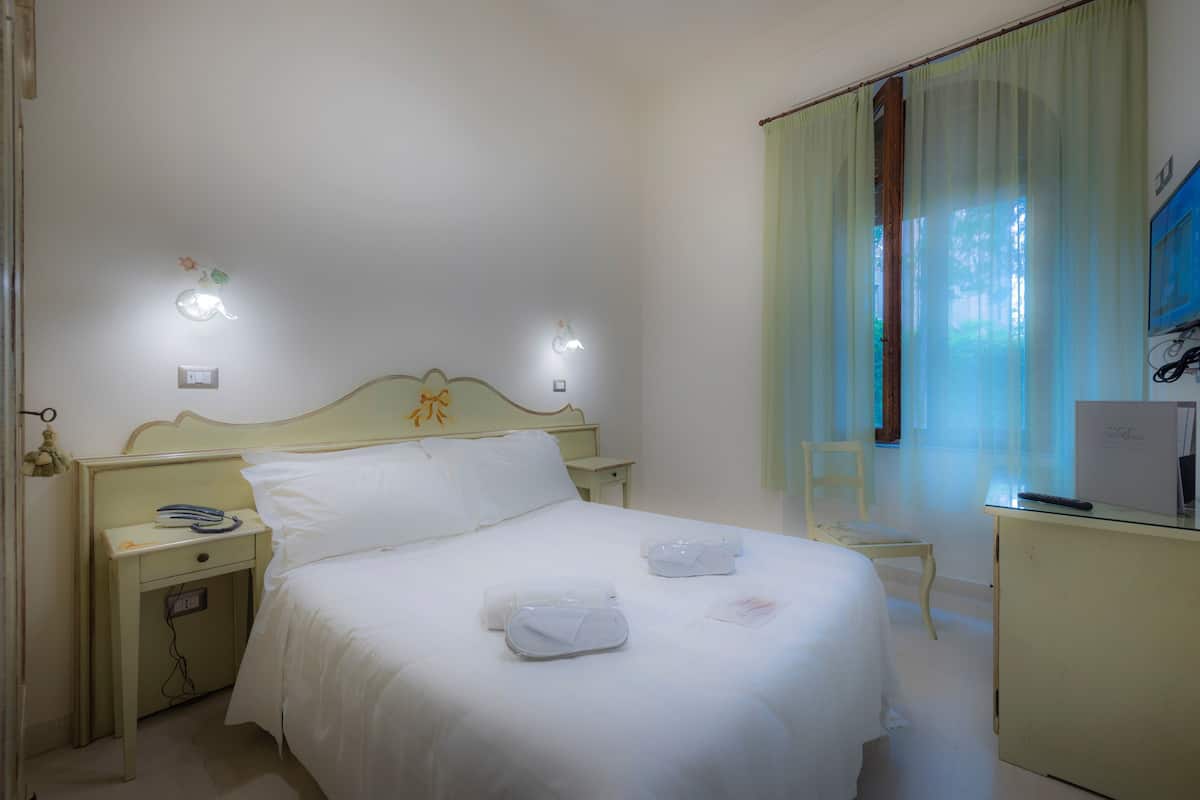 Une chambre d’hôtel avec un lit simple, deux tables de chevet, une petite table, un bureau et une chaise.
