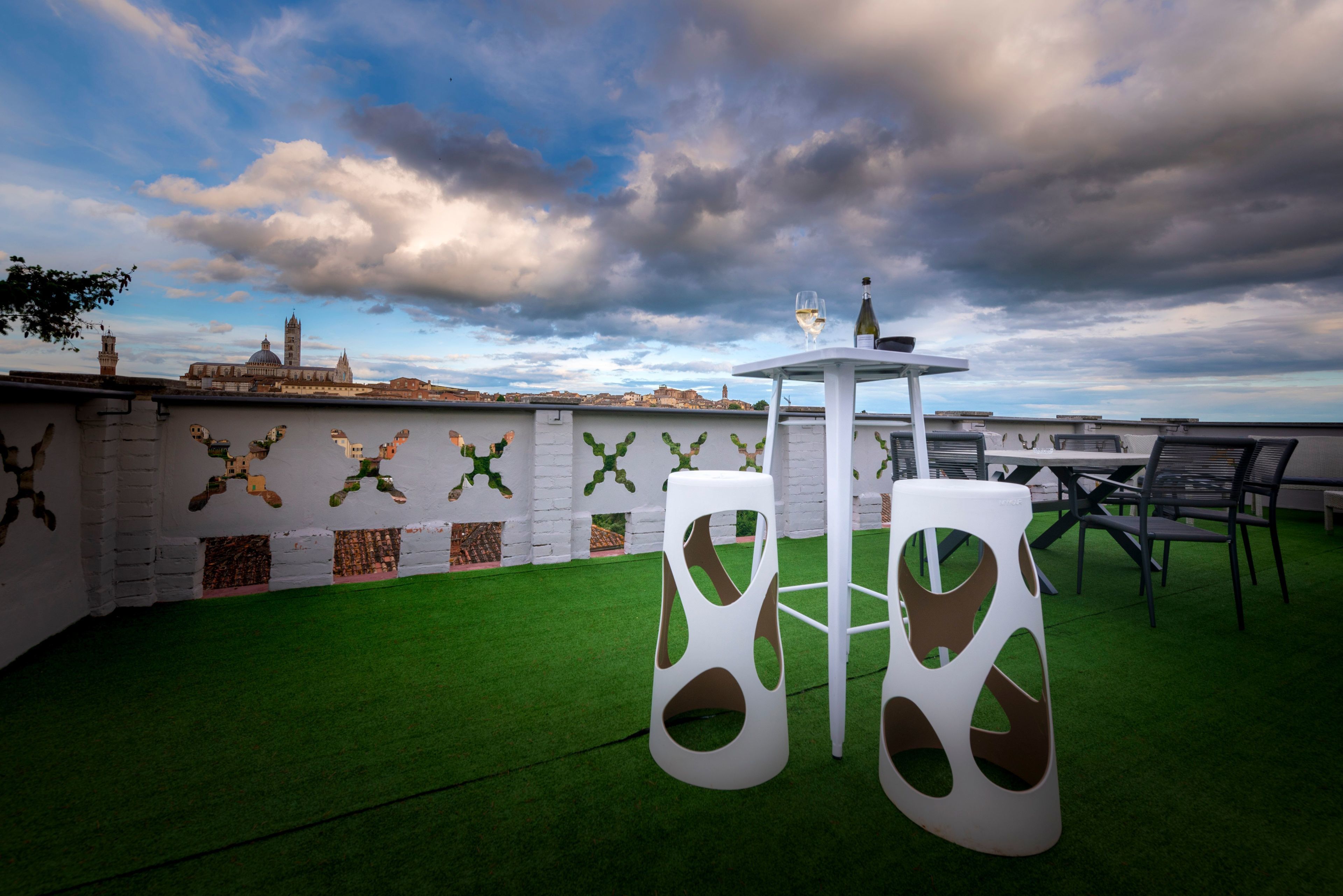 A rooftop terrace with a table and chairs, a bottle of wine, and a view of a historic building in the background.