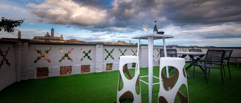 A rooftop terrace with a table and chairs, a bottle of wine, and a view of a historic building in the background.