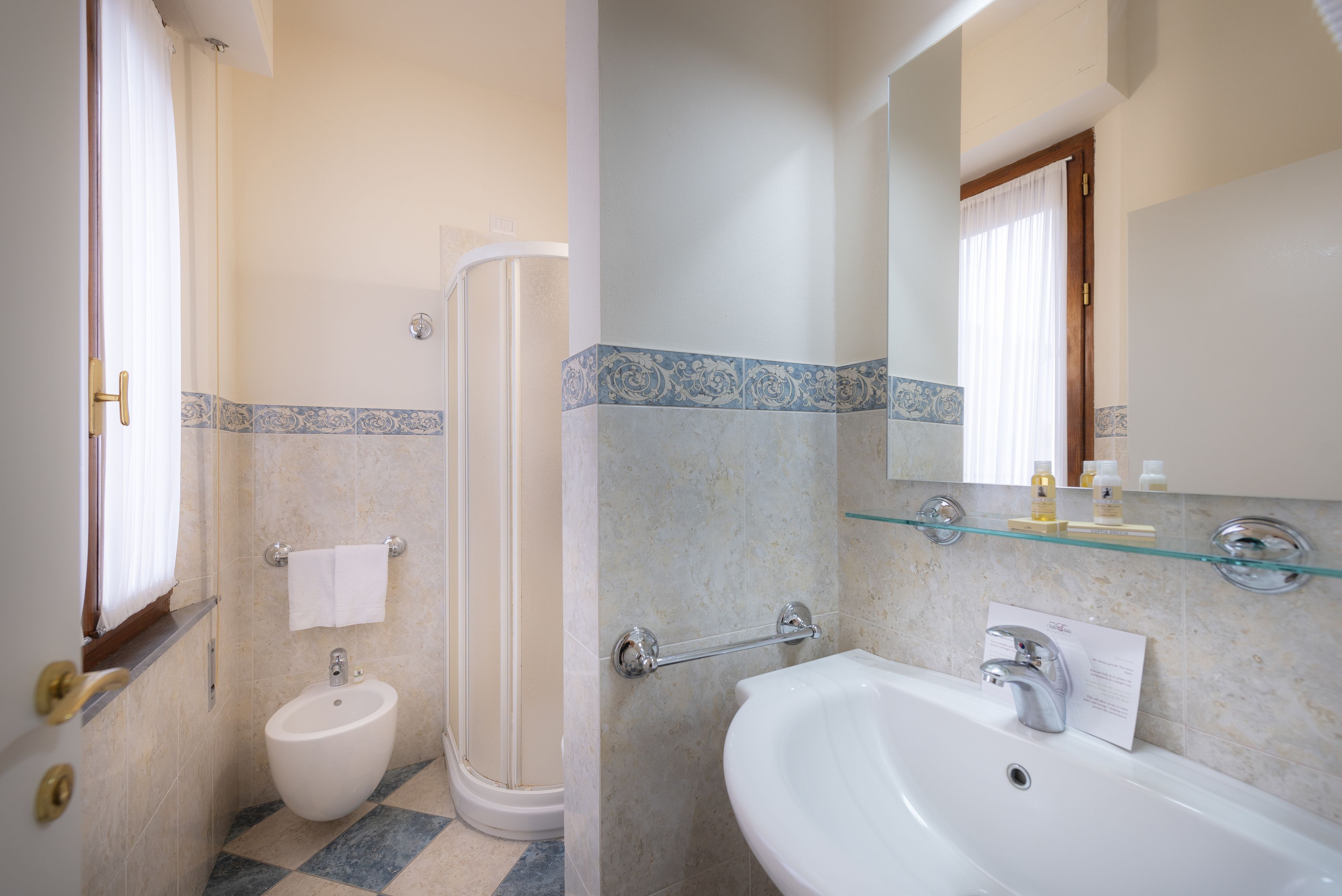 Een badkamer met een bidet, een glazen plank met toiletartikelen en een spiegel boven de wastafel.