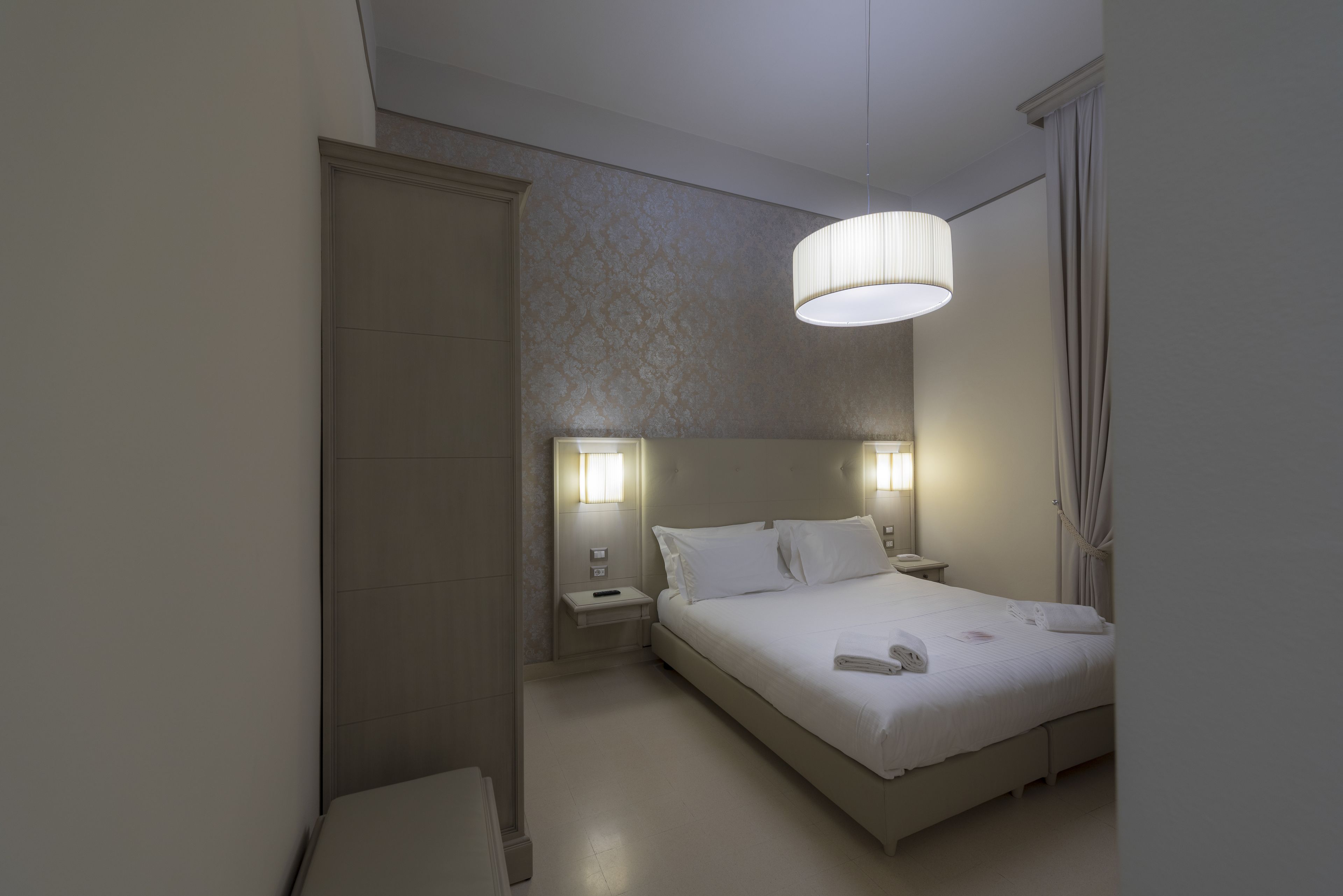 Ein modernes Hotelzimmer mit einem großen Bett, Nachttischlampen, einem Nachttisch und einem Kleiderschrank.