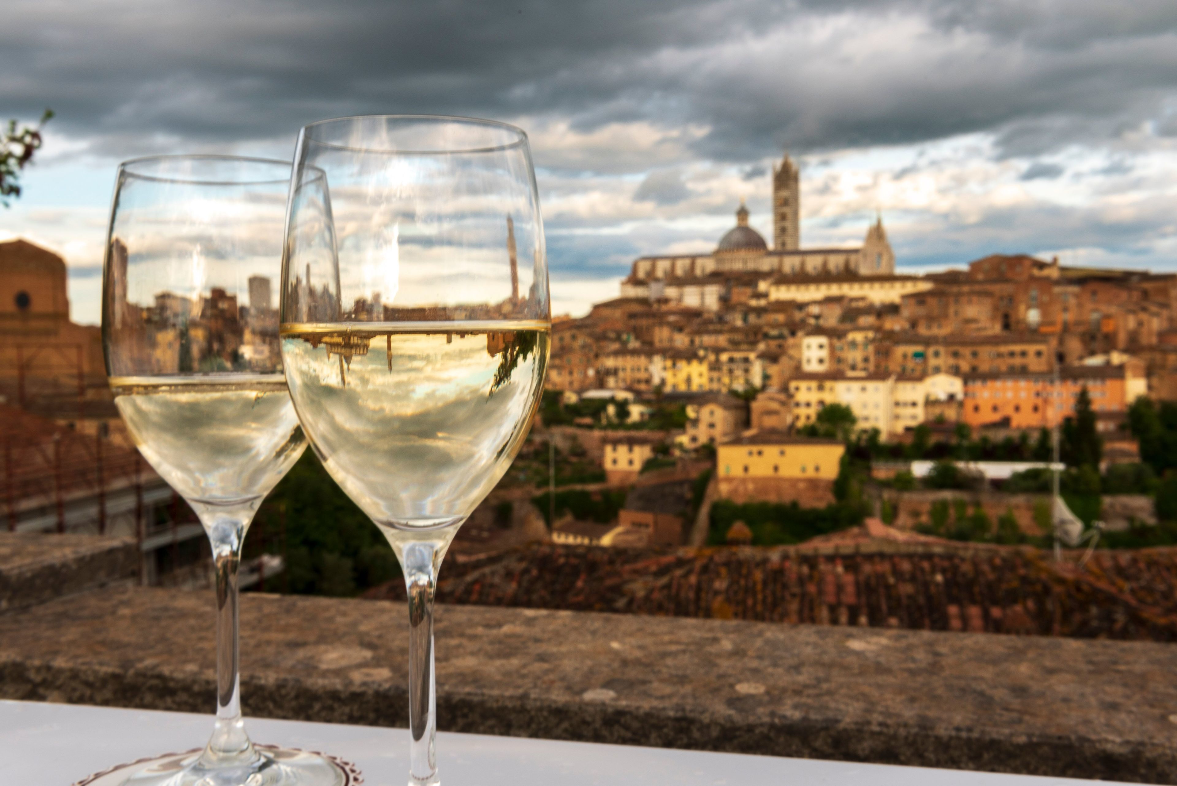 Two glasses of white wine on a table with a view of a historic cityscape in the background.