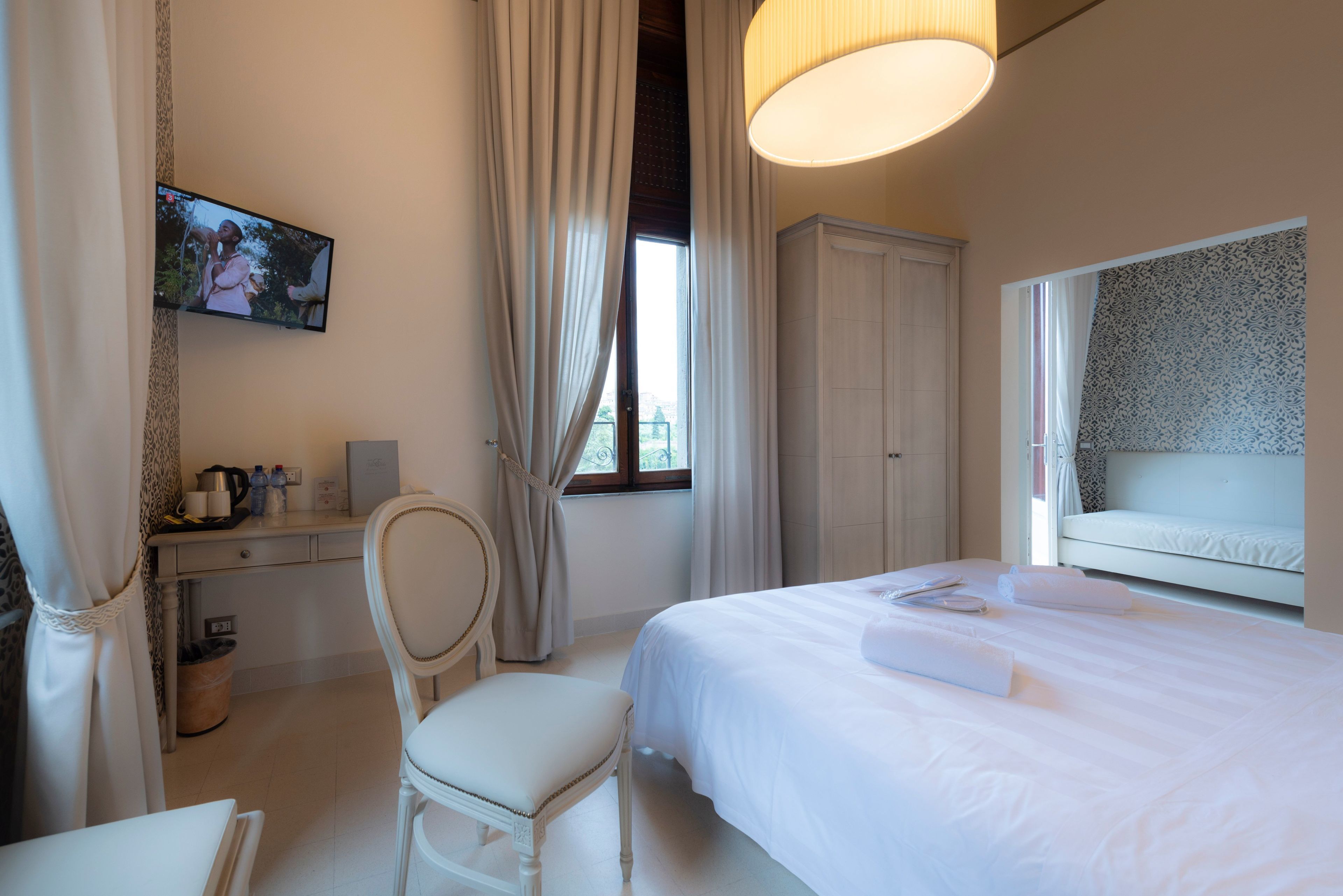 Habitación de hotel con cama, escritorio, silla, televisión y ventana con cortinas.