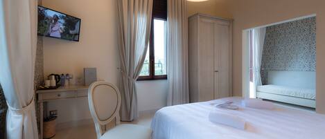 Habitación de hotel con cama, escritorio, silla, televisión y ventana con cortinas.