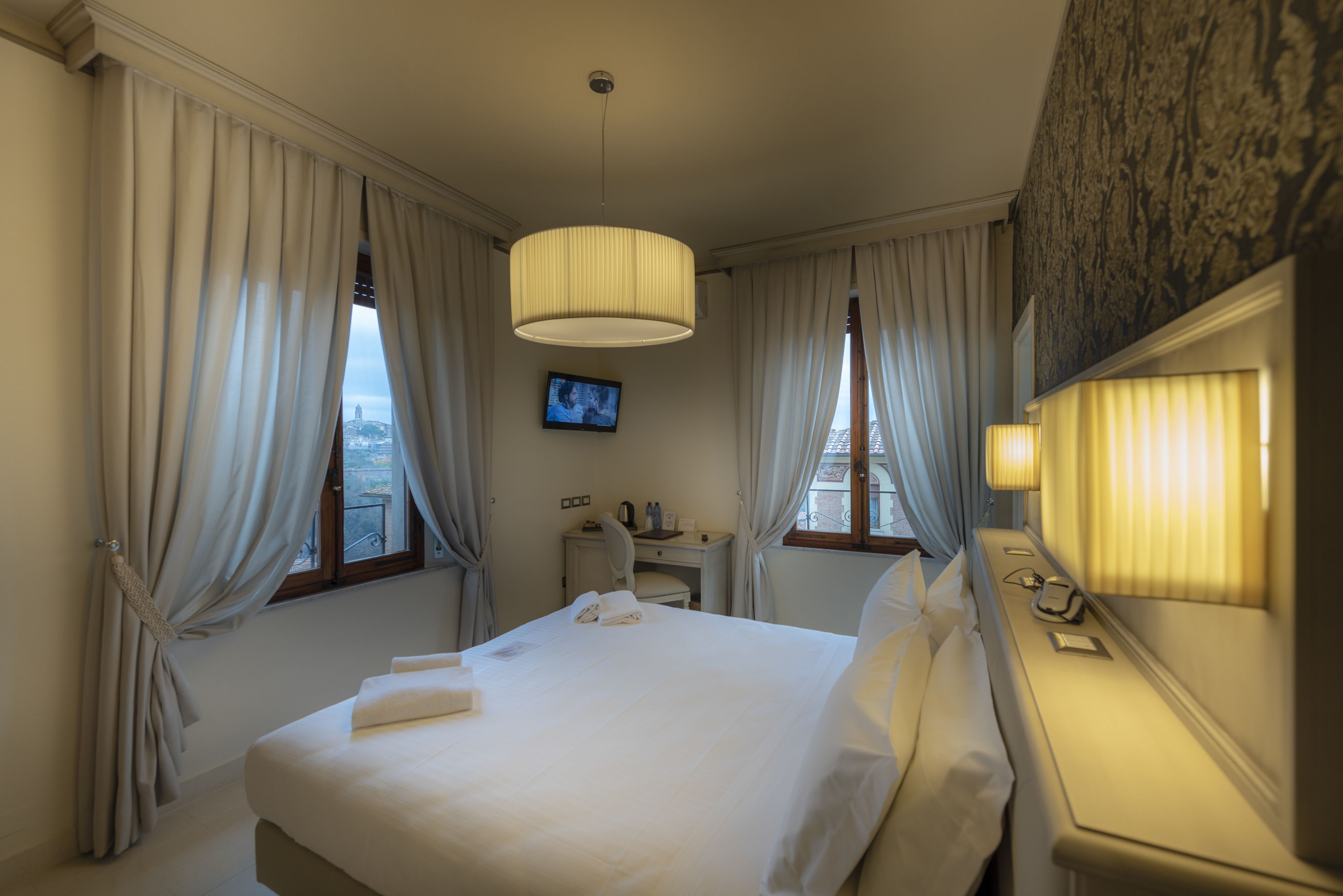 Une chambre d’hôtel avec un grand lit, un bureau avec une chaise, un téléviseur fixé au mur et des rideaux aux fenêtres.