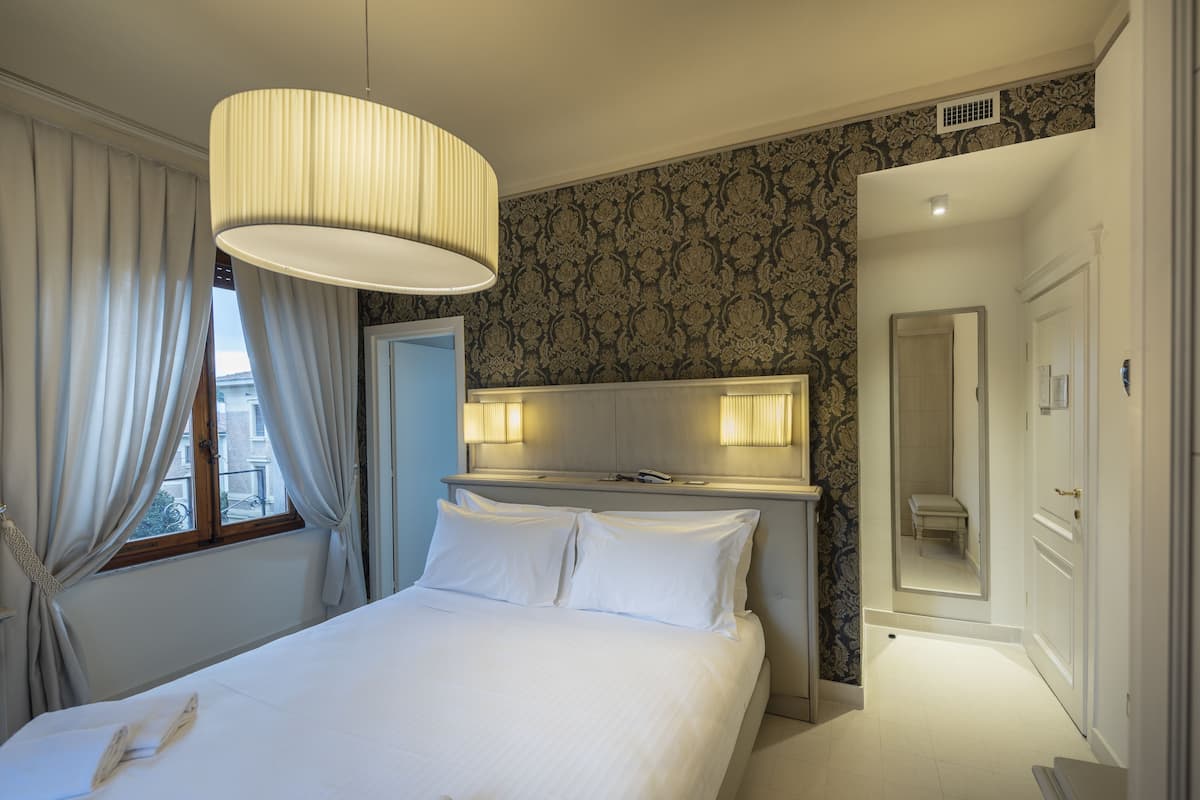 Une chambre d’hôtel avec un grand lit, une table de chevet, un miroir et une fenêtre avec des rideaux.