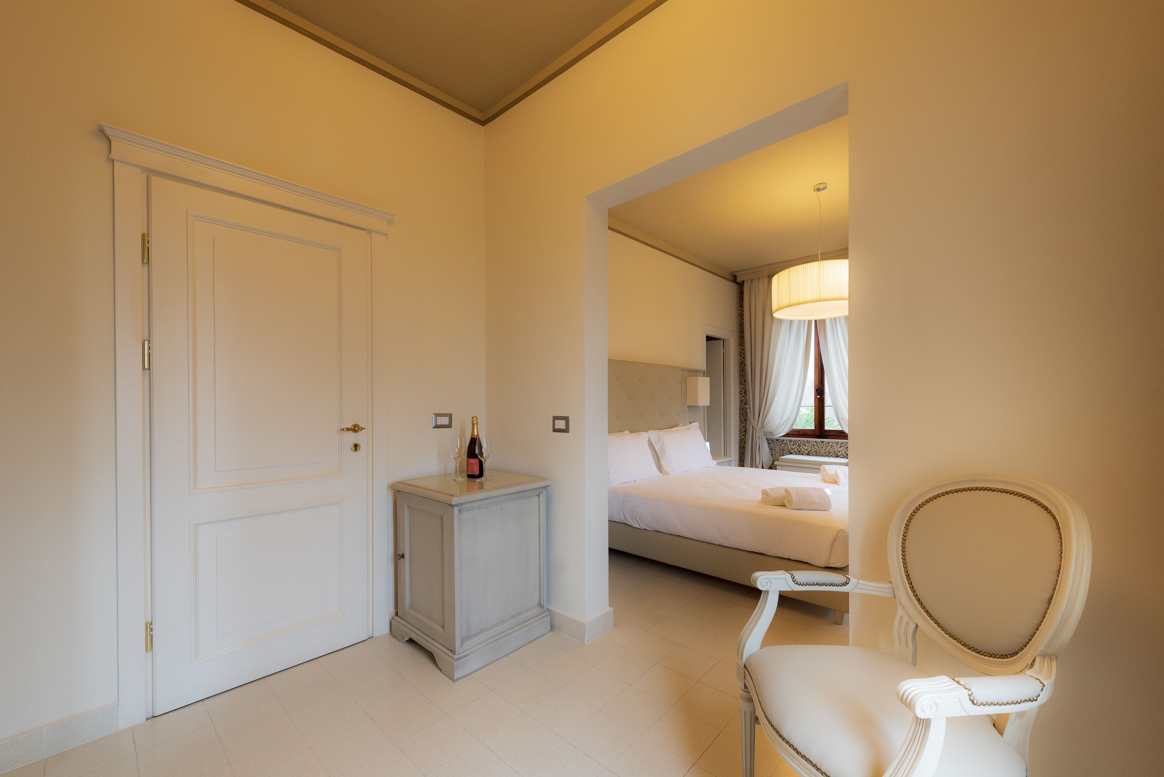 A hotel room with a bed, a chair, a nightstand, and a door.