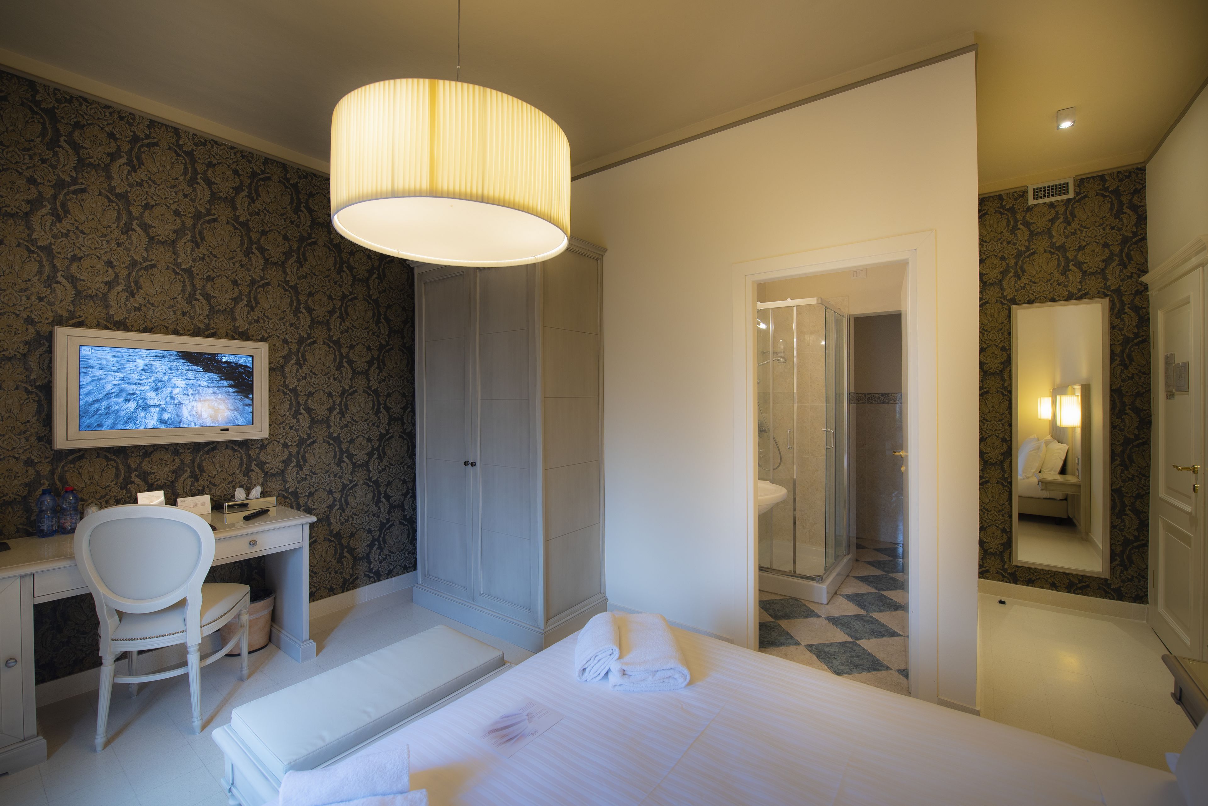 Habitación de hotel con cama, escritorio, silla, televisión, ducha y espejo.