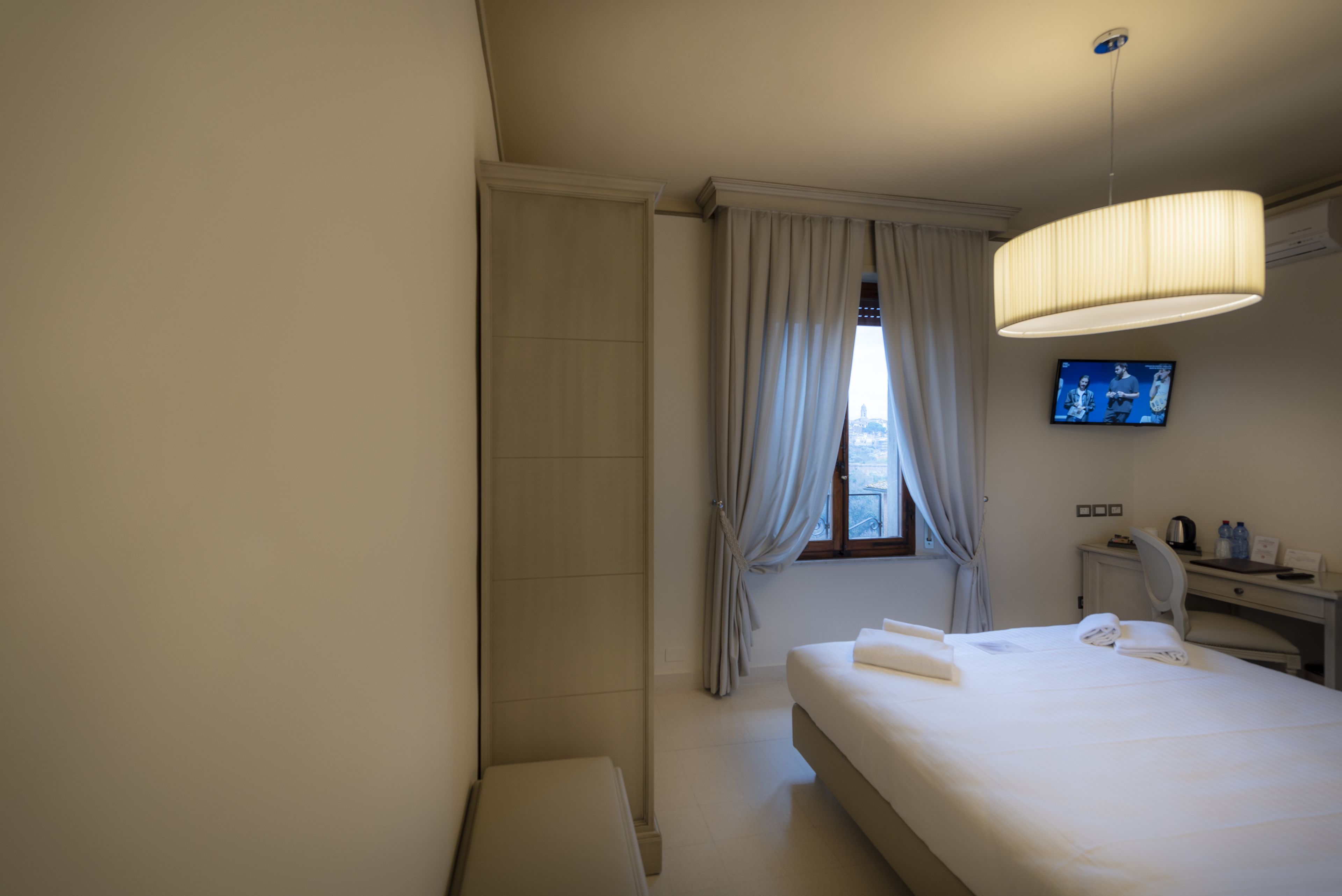 Una habitación de hotel con cama, escritorio, silla, televisión y ventana con cortinas.