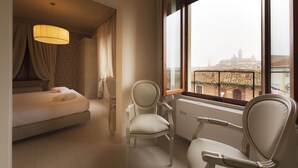 Een hotelkamer met een bed, twee stoelen, een raam met uitzicht op een stadsbeeld en een radiator.
