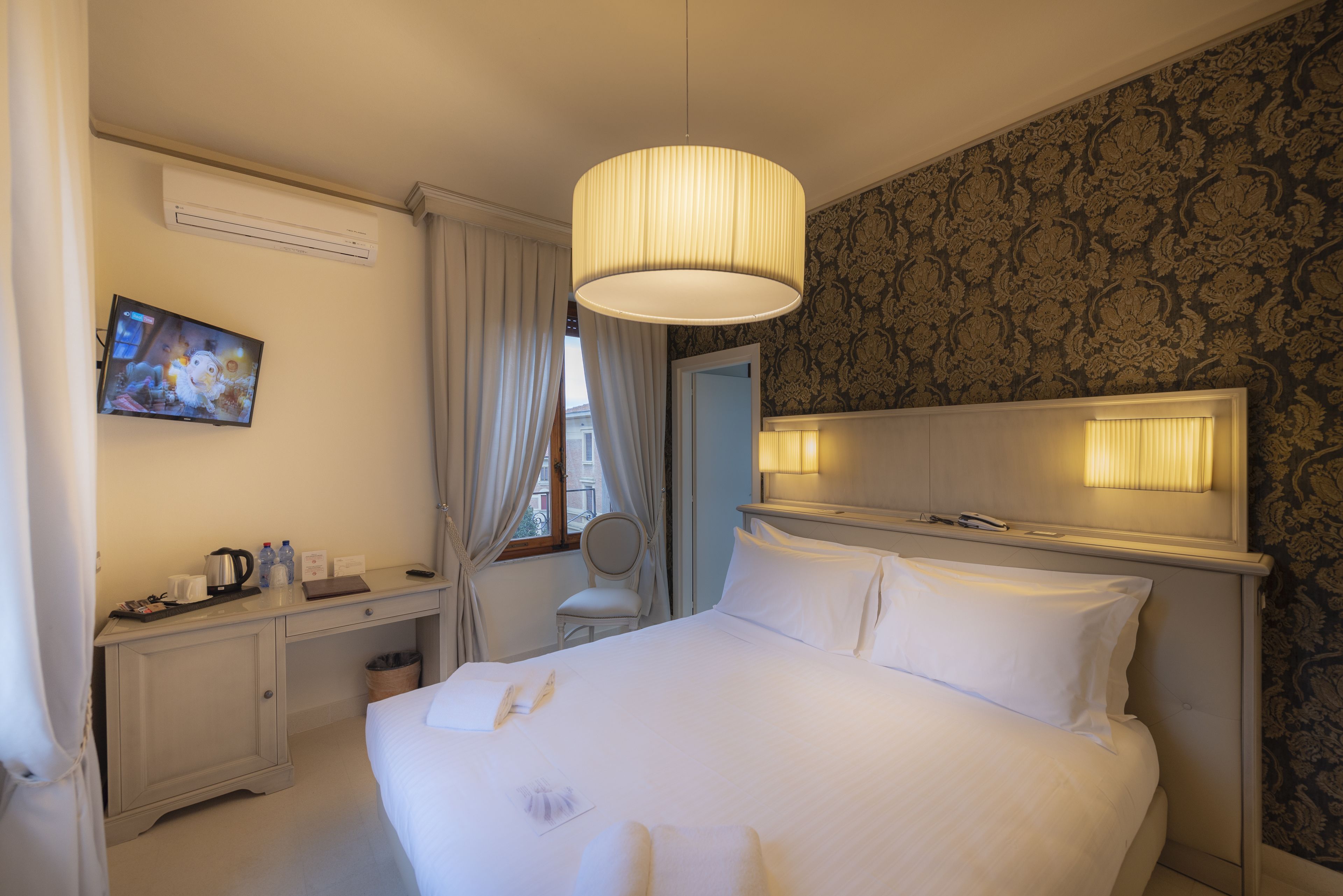 Een hotelkamer met een bed, een bureau, een stoel, een televisie en een raam met gordijnen.