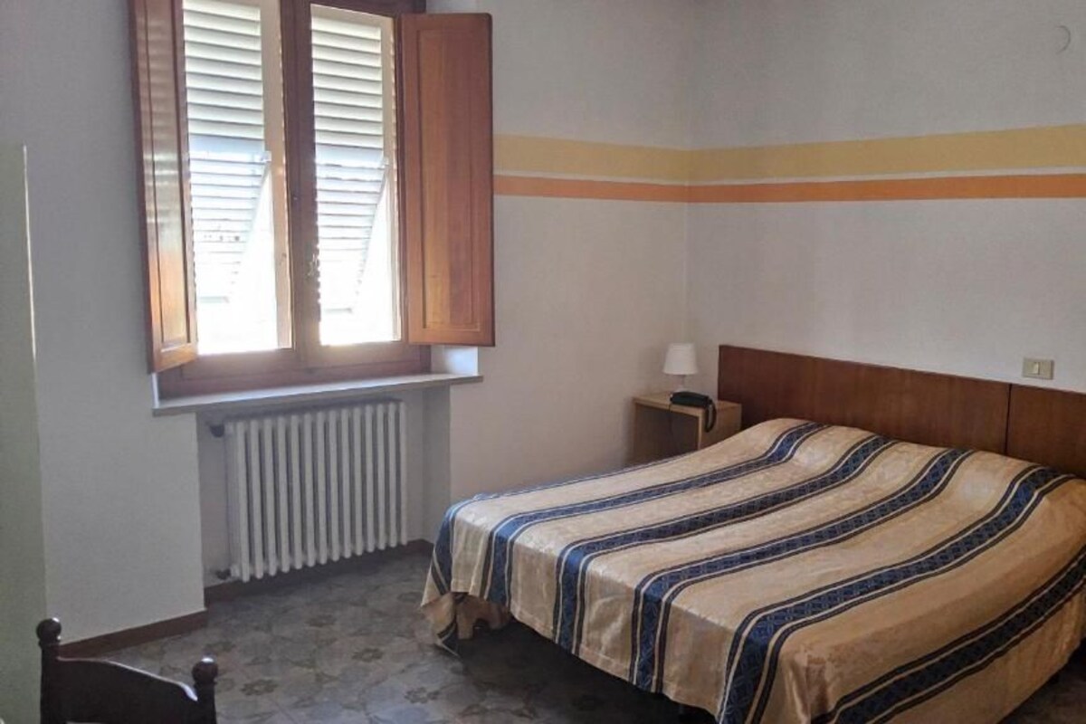 A bedroom with a bed, a nightstand, a window with blinds, and a radiator.