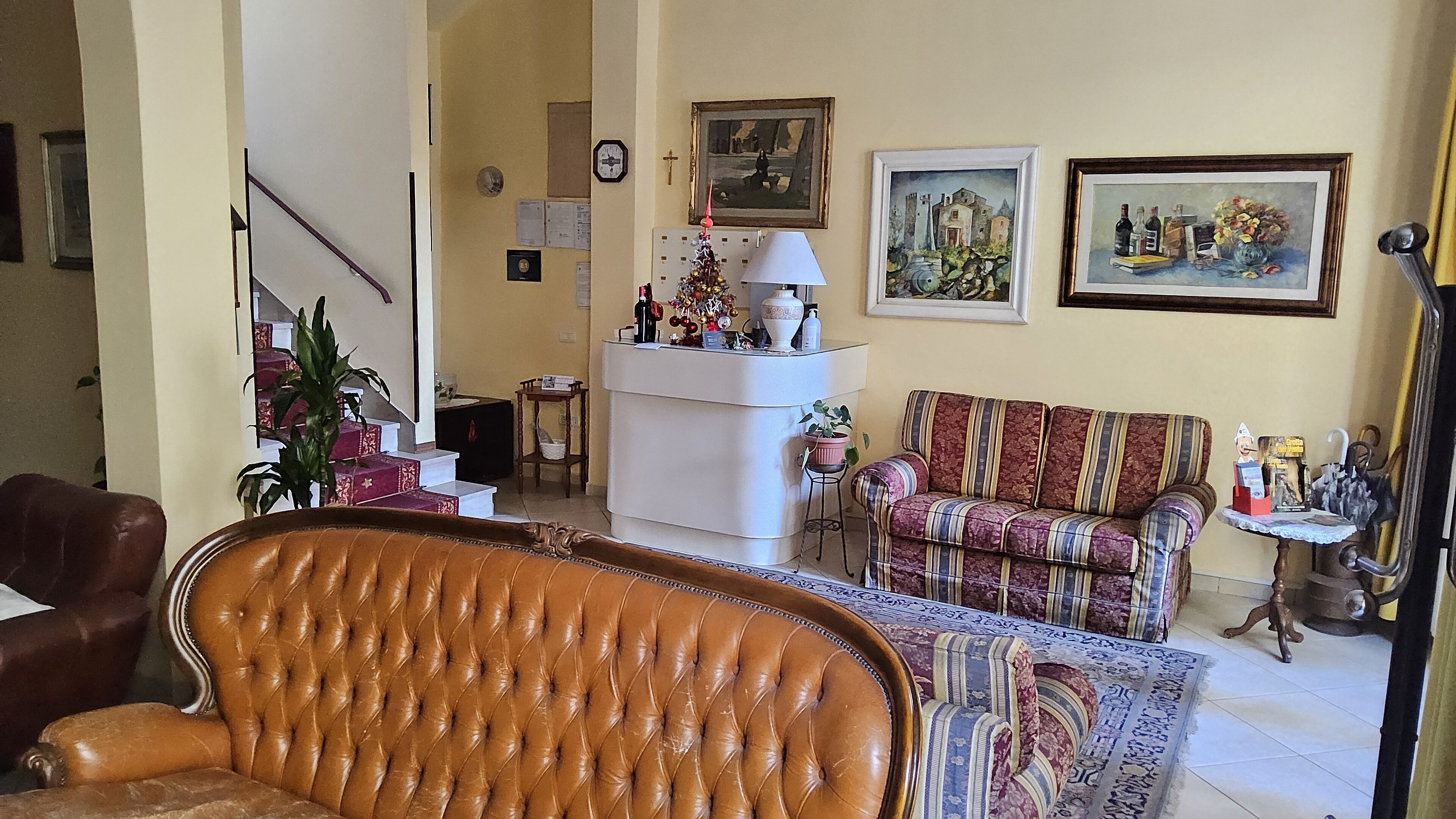 A living room with a brown leather sofa, a patterned armchair, a white console table with decorative items, and two framed paintings on the wall.