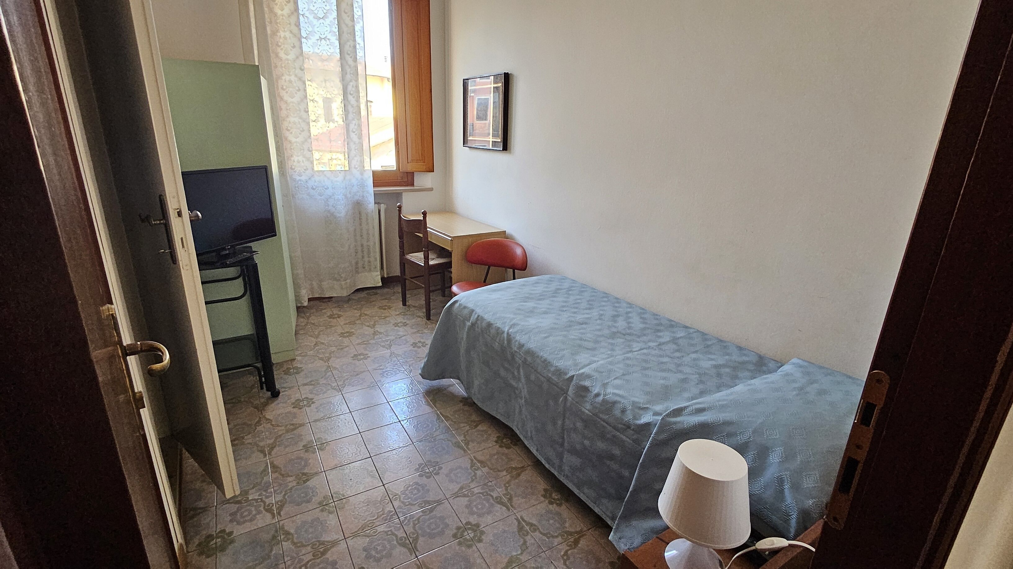 Une petite pièce, de taille modeste, comprenant un lit, un bureau, une chaise et un téléviseur.