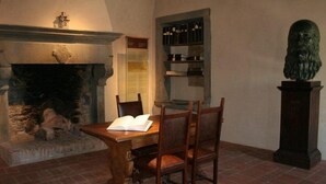 A room with a fireplace, a wooden table with chairs, a bookshelf, and a bust statue. - Verena (Montecatini Terme)