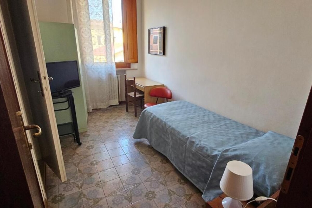 Una habitación pequeña y funcional con cama, escritorio, silla y televisión.