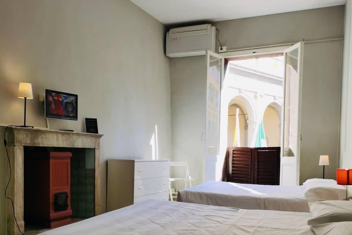 A hotel room with two beds, a fireplace, a television, and an open door leading to a courtyard with arches.