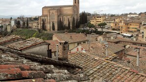 A historic building with a prominent tower, surrounded by traditional buildings with terracotta roofs. - La Perla (Siena)