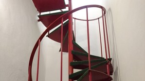 A spiral staircase with red railings and green steps against a plain wall. - La Perla (Siena)