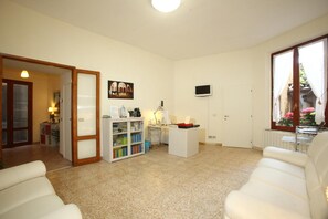 A living room with a white sofa, a coffee table, a TV mounted on the wall, and a door leading to another room. - La Perla (Siena)