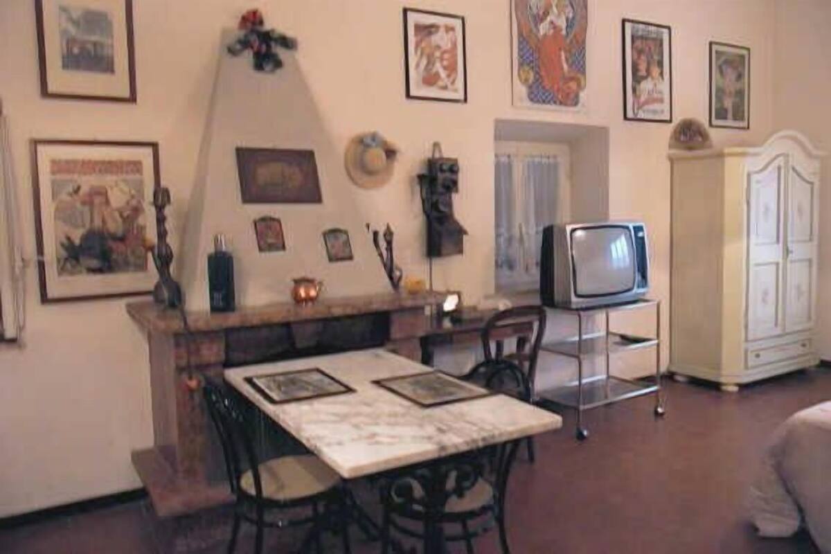 A living room with a dining table, chairs, a television, and various framed pictures on the walls.