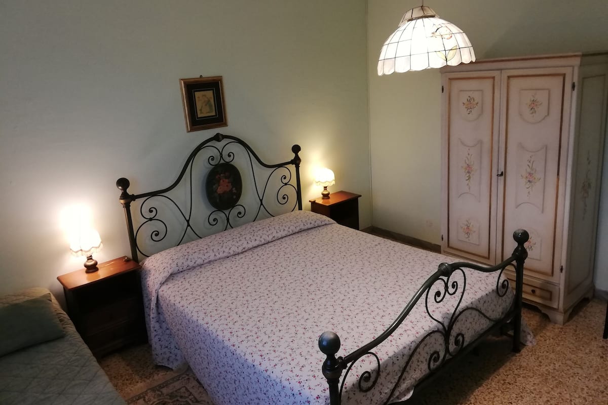 A bedroom with a bed, two bedside lamps, a nightstand, a wardrobe, and a hanging light fixture.