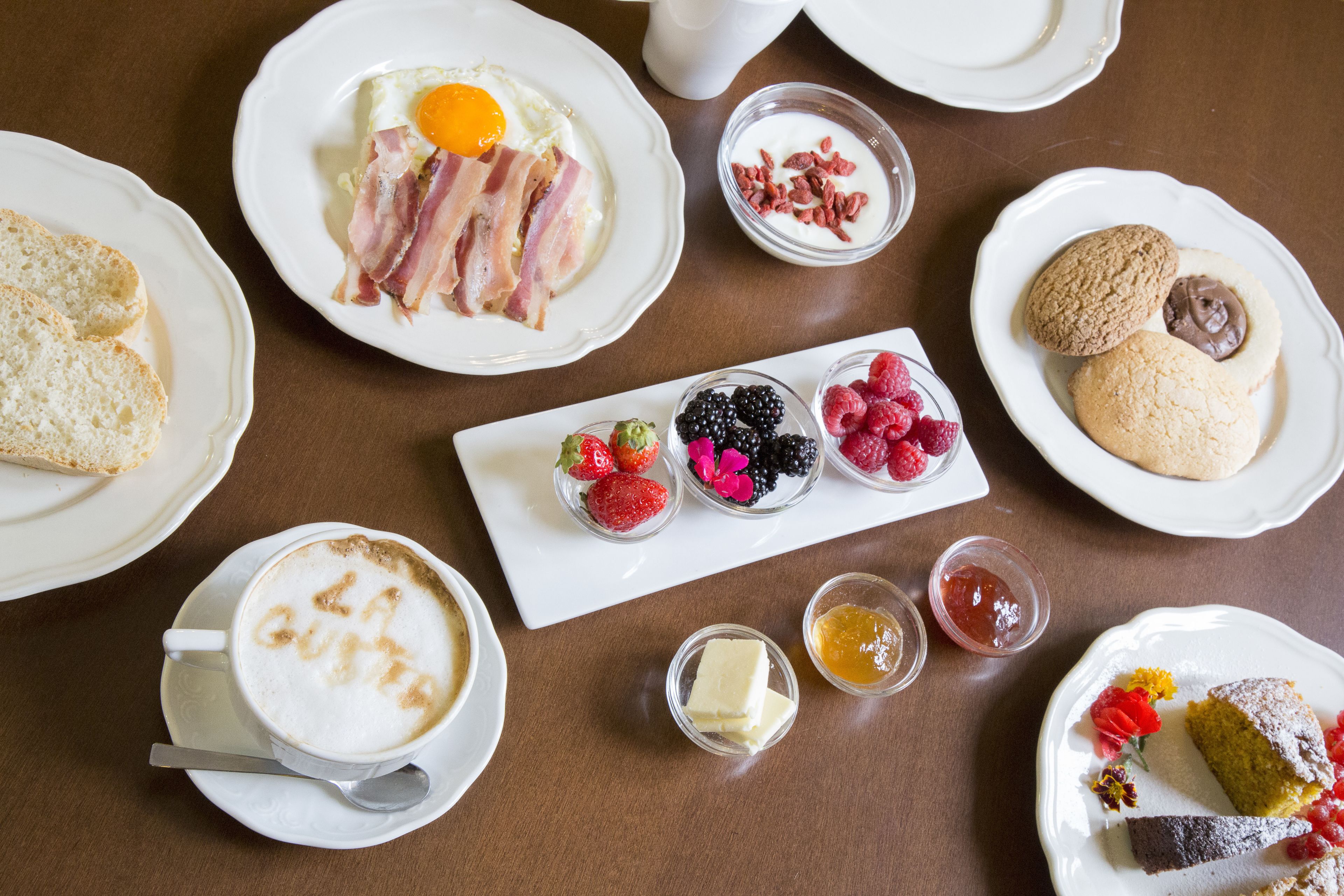 A breakfast setting with various dishes including toast, eggs, bacon, berries, and pastries.