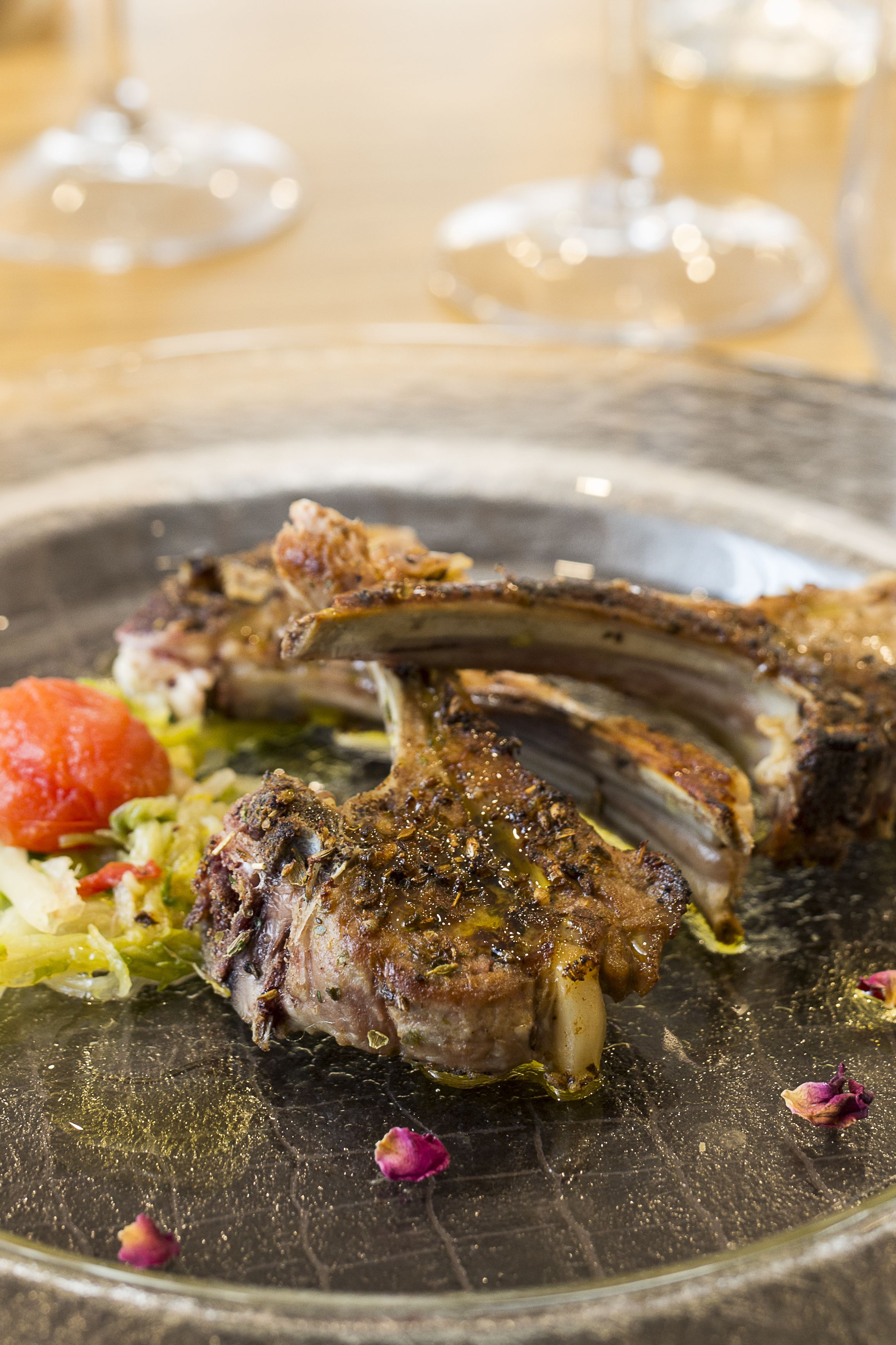 Ein Nahaufnahme einer Speise mit Lammkoteletts, einem gemischten Salat und einer kleinen Tomate.