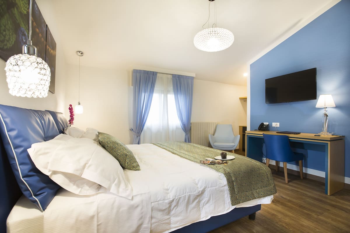 A bedroom with a bed, a desk, a chair, a TV, and a lamp.