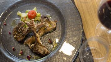 A plate of food with lamb chops and vegetables, accompanied by a glass of red wine.