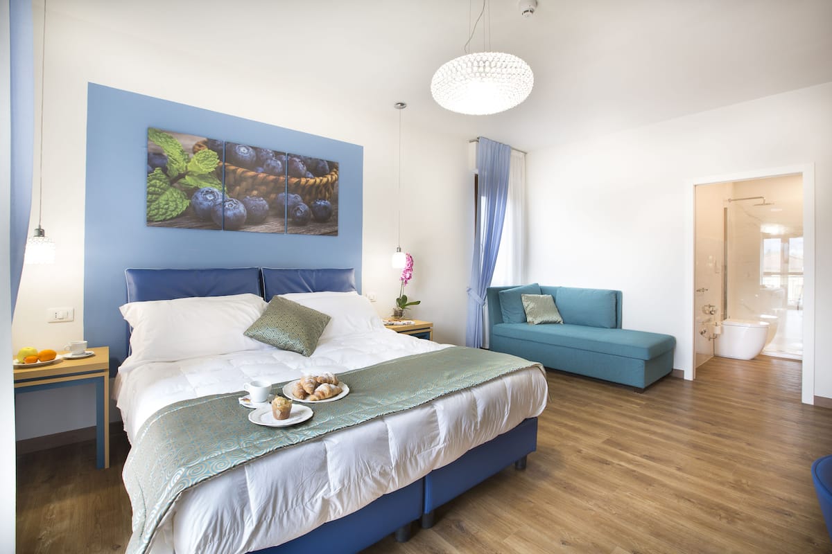A modern bedroom with a large bed, a blue sofa, and a breakfast setup on the side.