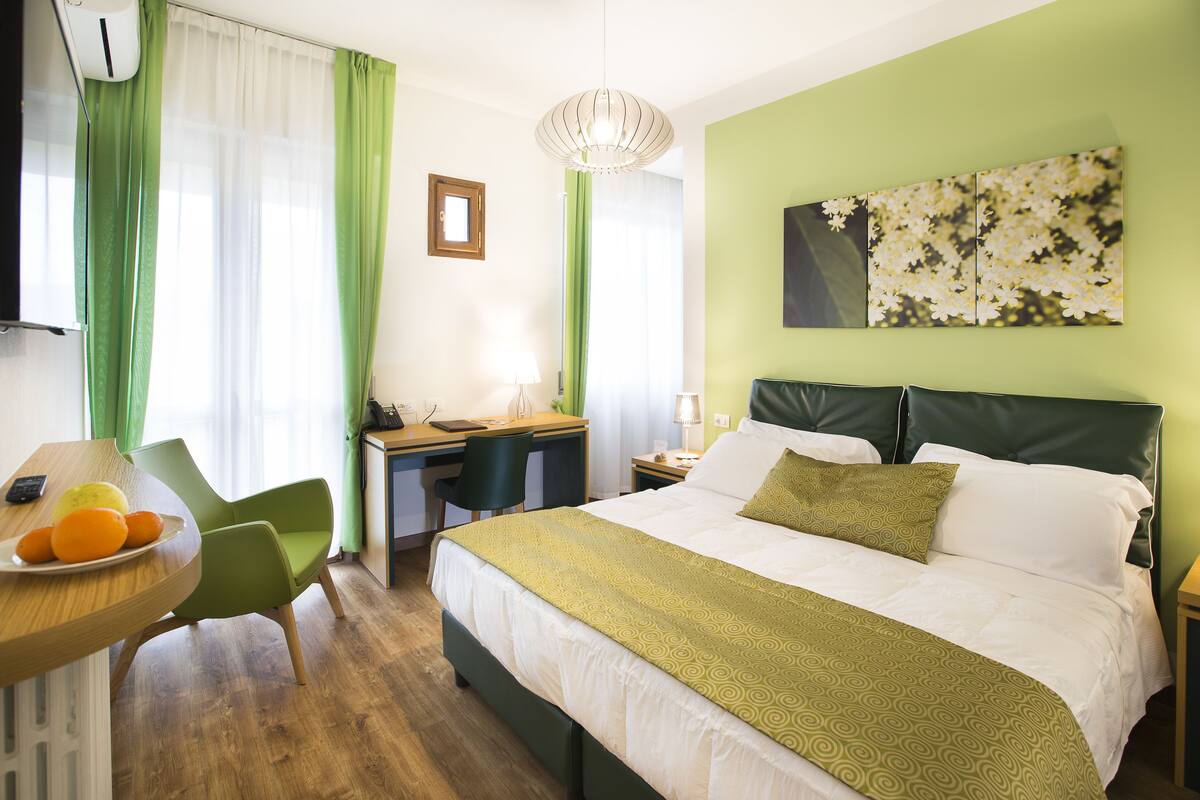 A hotel room with a bed, desk, chair, and a fruit bowl.