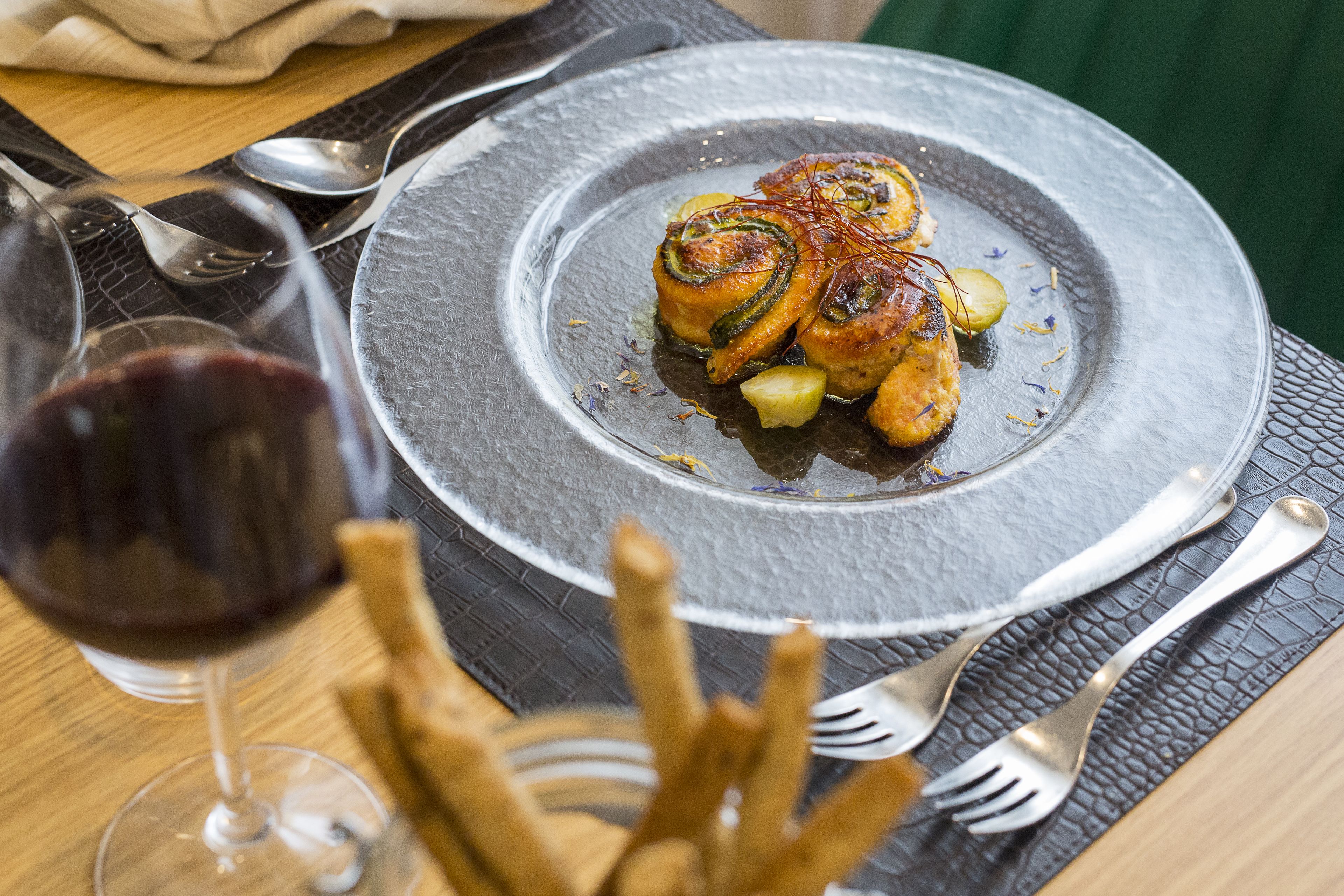 A dining table with a plate of food, cutlery, and a glass of red wine.