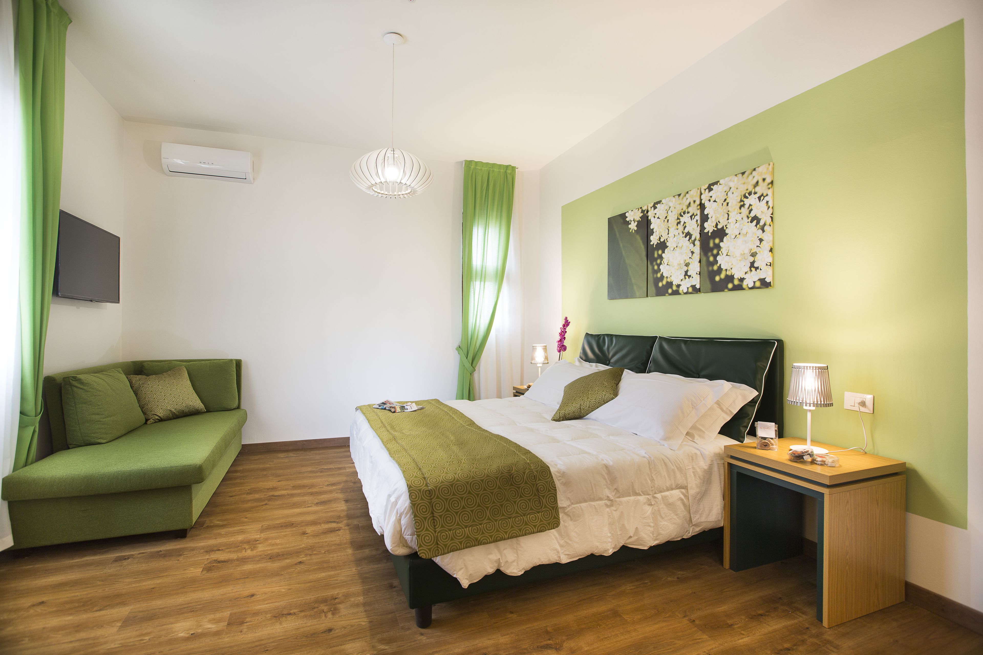 A bedroom with a bed, a green sofa, a bedside table, and a wall-mounted air conditioner.