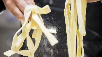Mani che tengono pasta, con farina che viene sparsa sopra.
