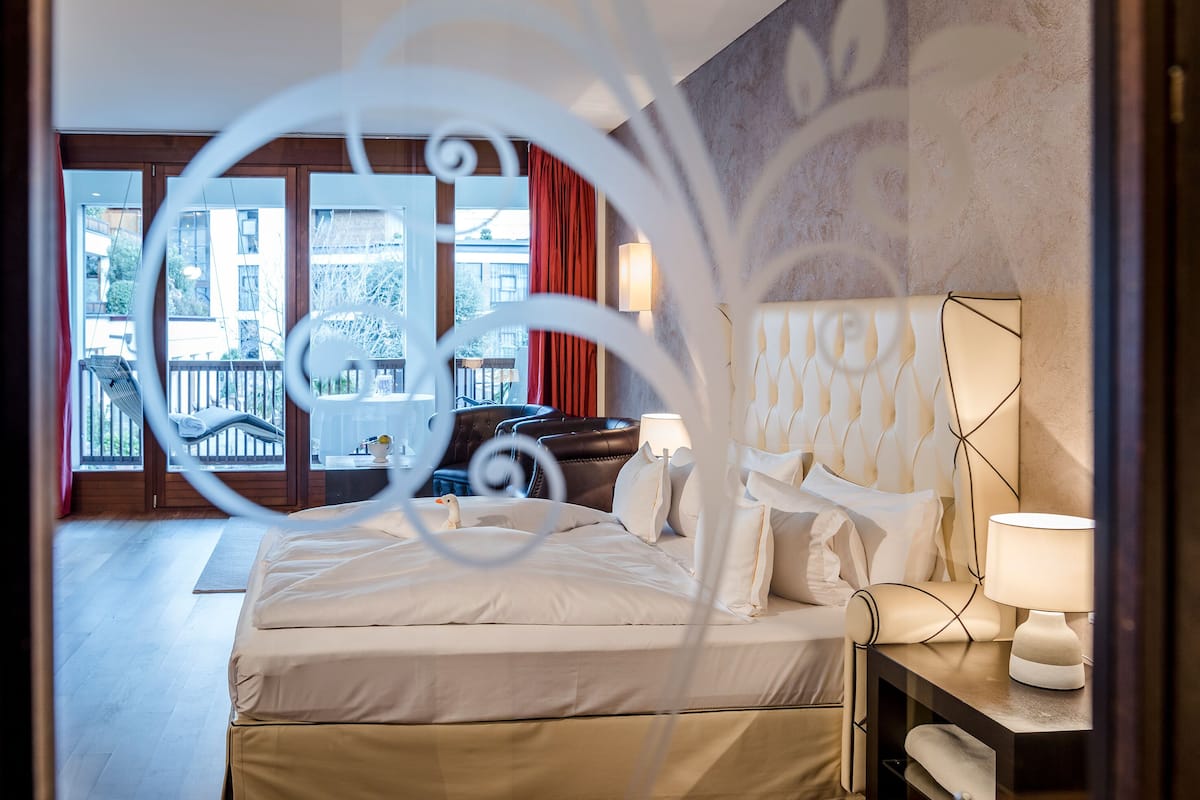 A hotel room with a bed, a nightstand, a lamp, and a view of the outside balcony.