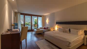 A modern hotel room with a large bed, a desk, a chair, a sofa, and a balcony with a view of the mountains.