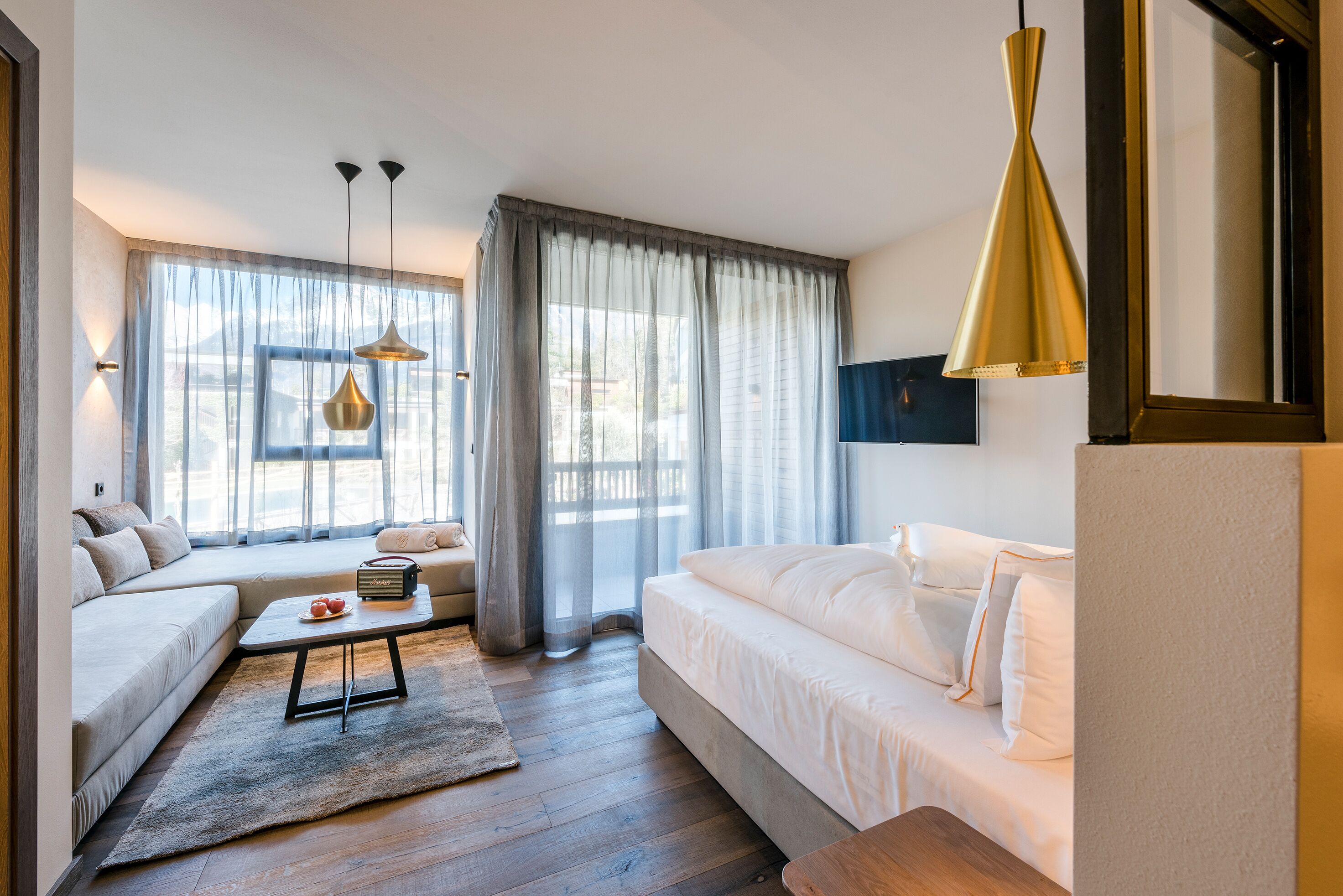 Una habitación de hotel moderna con sofá, cama, una mesita de centro y un ventanal con cortinas.