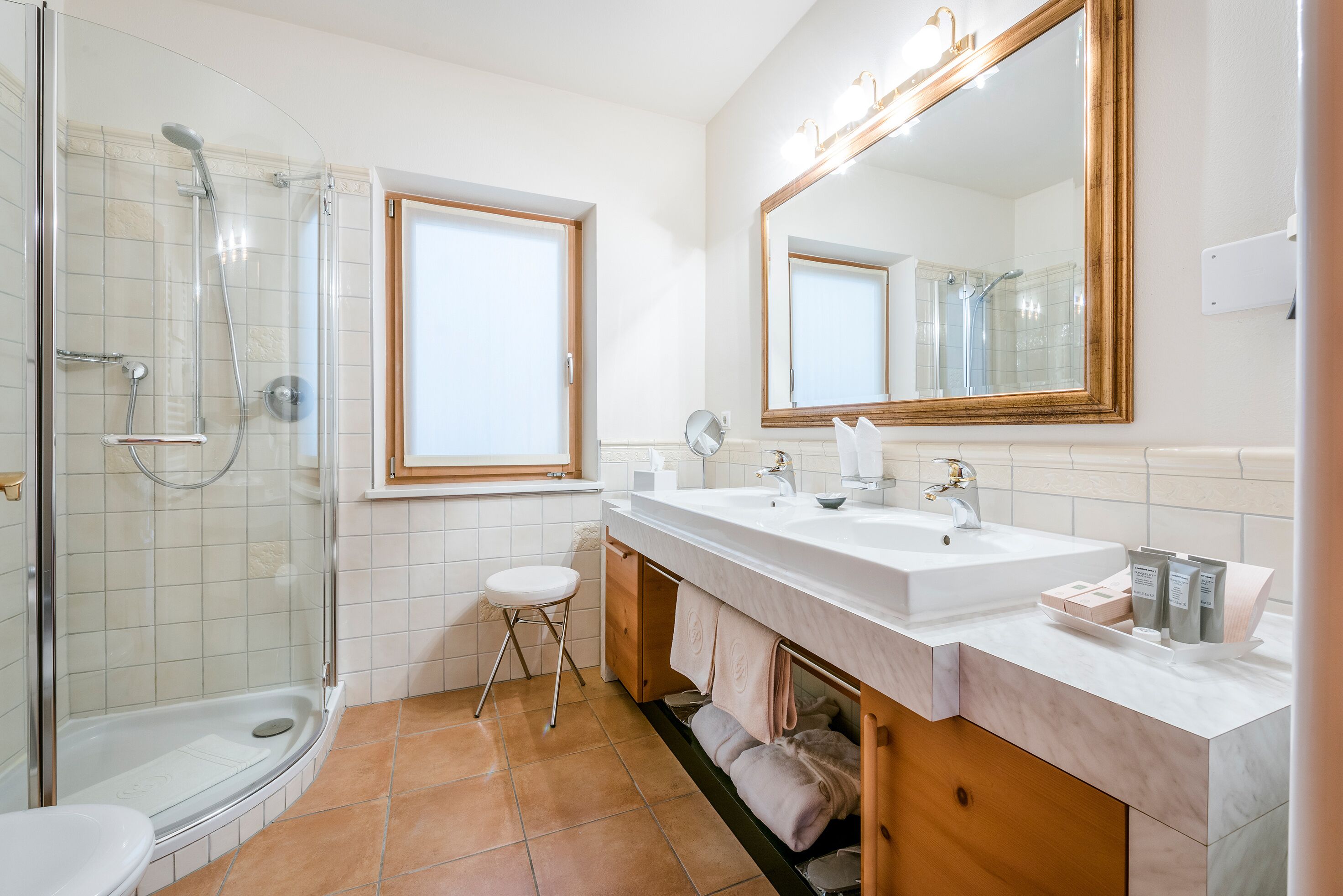 Un baño moderno con ducha envuelta en vidrio, dos lavamanos, un espejo grande y una ventana.